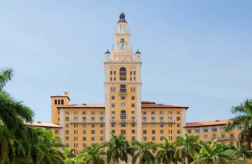 A large building with a clock tower and palm trees in front of it.