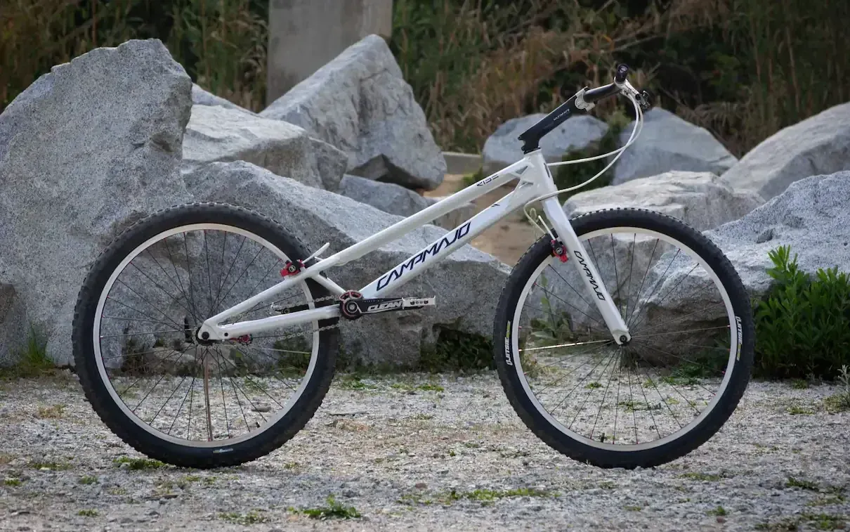 Witte mountainbike met zwarte wielen, leunend op grind naast grote rotsen in de buitenlucht.