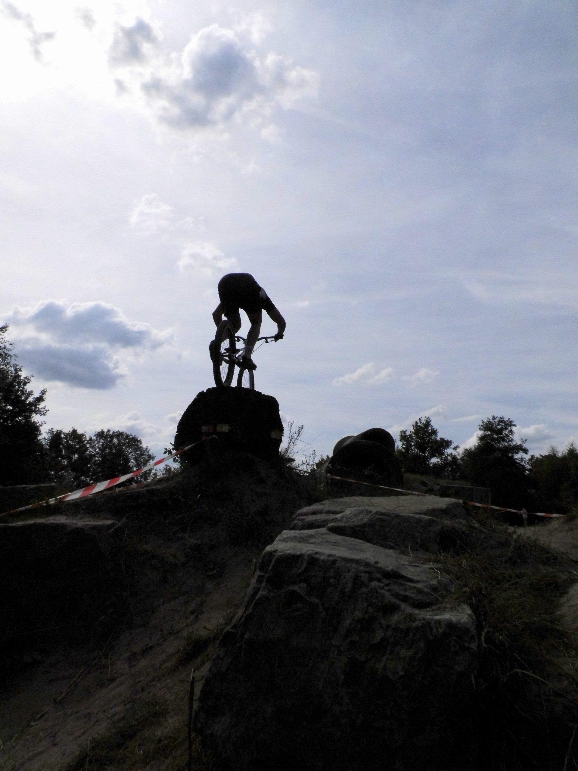 Silhouet van een klimmer op een rotsachtig uitsteeksel onder een heldere, bewolkte hemel.