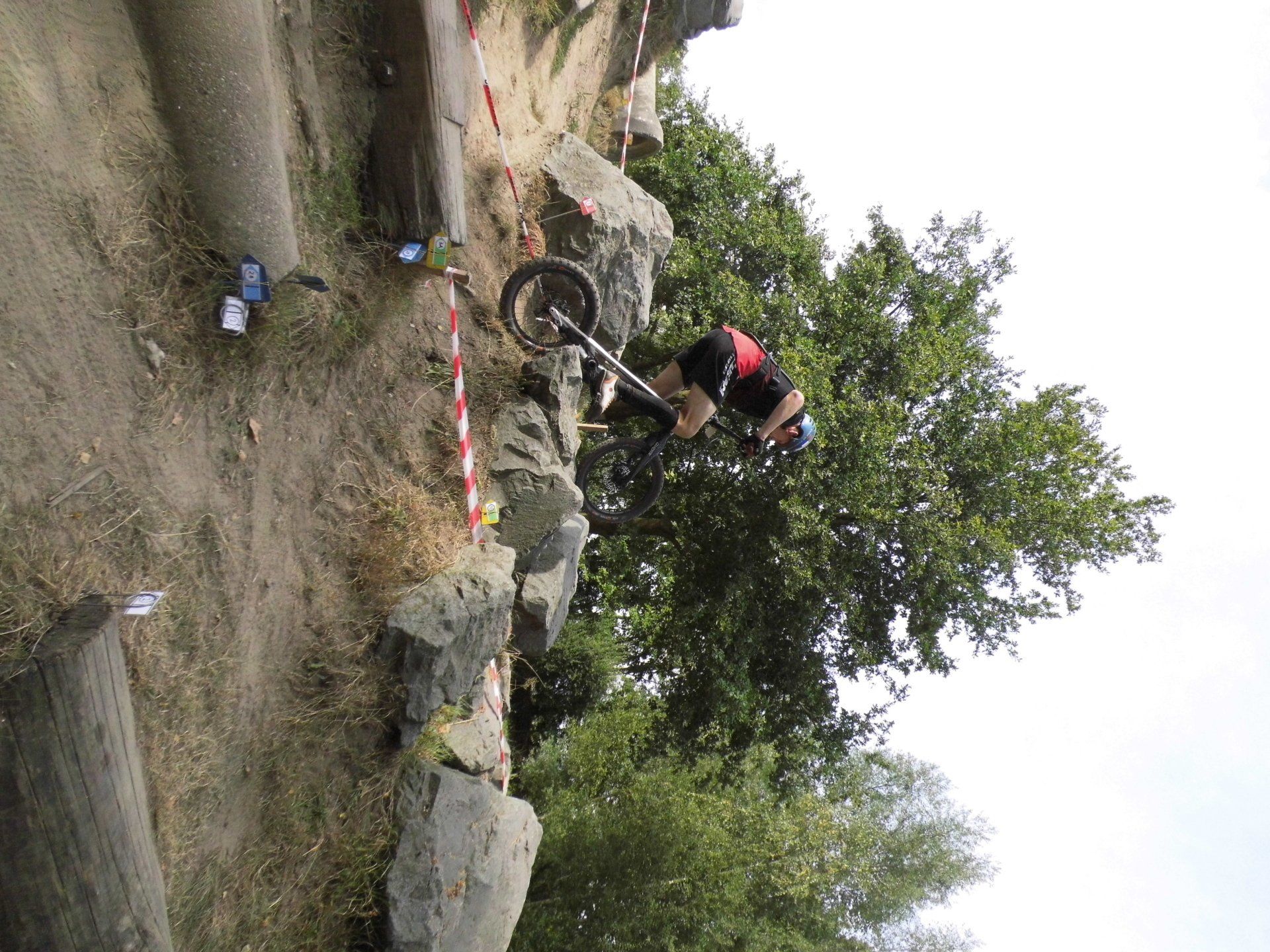 Fietsers op een ruig onverhard pad langs rotsen en bomen, met rood-wit afzetlint dat het pad markeert.