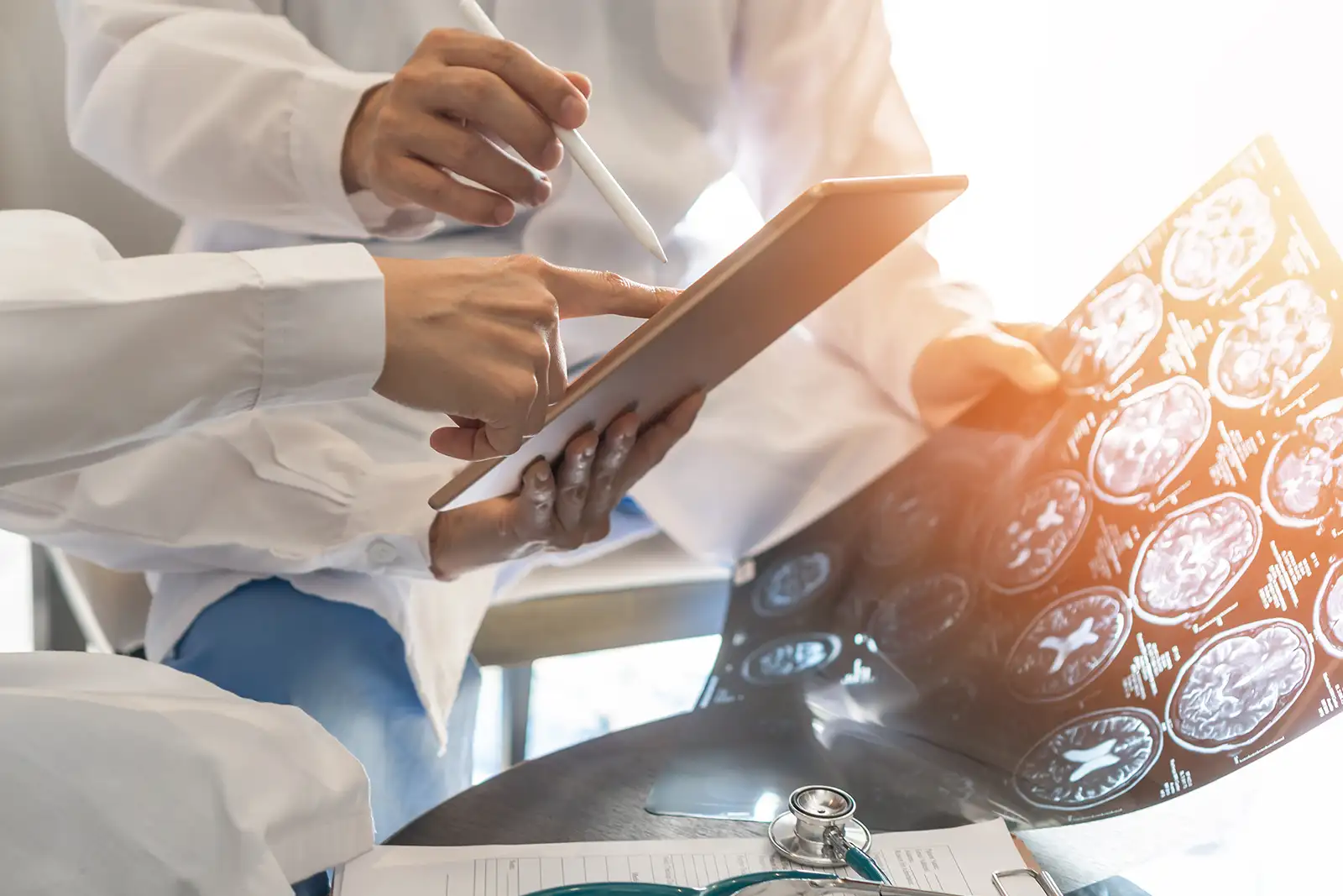 Two doctors reviewing a tablet beside X-ray films in a bright hospital setting