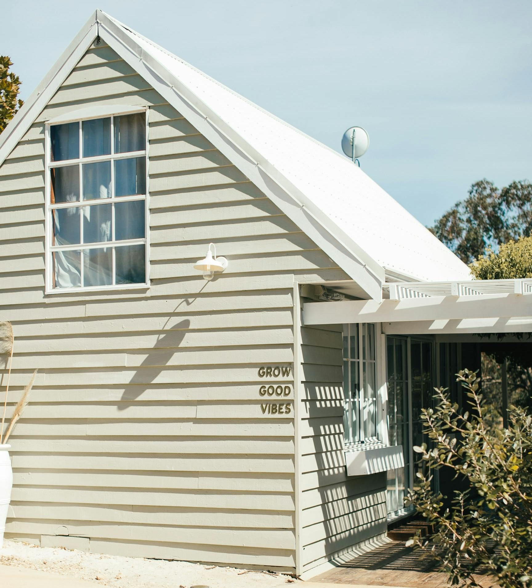 A light sage green cabin with a white roof and a sign on the exterior wall that reads 