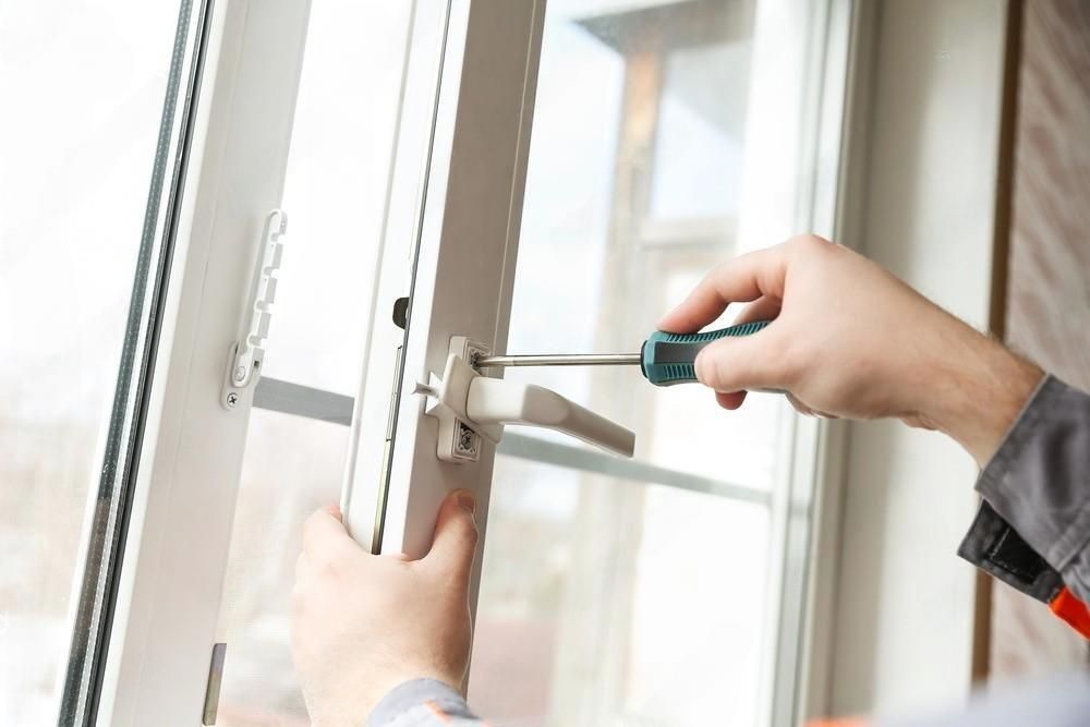 A close-up view of hands using a screwdriver to adjust or install a handle on a white uPVC window frame.