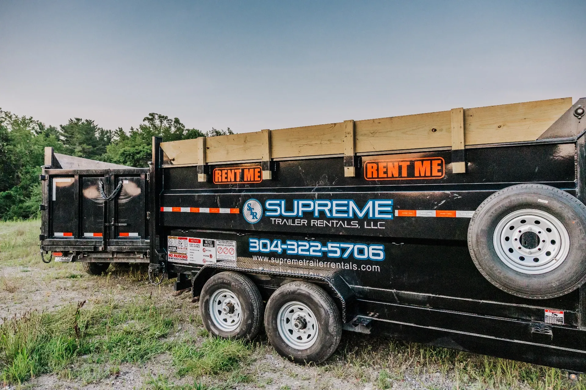 Black Supreme roll-off dumpster trailer on grass, with