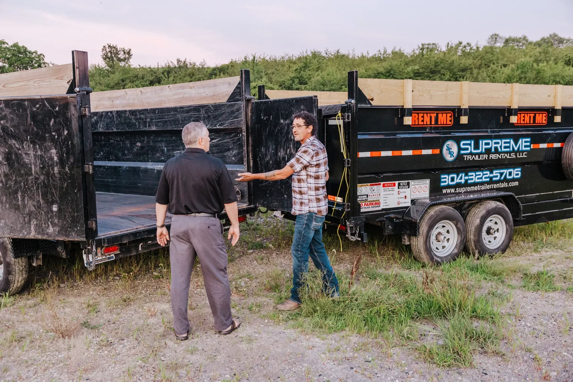 Two men beside open black dump trailers with 