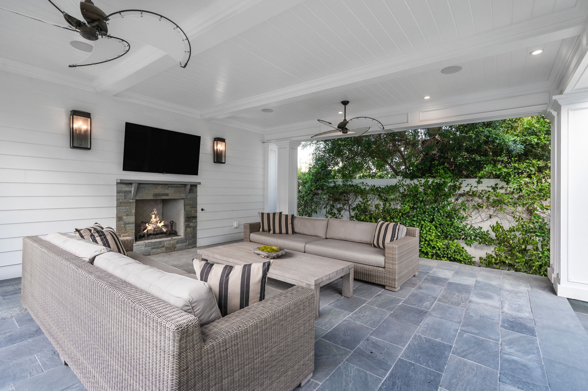 Covered patio lounge with gray sectional, fireplace, TV, and greenery wall