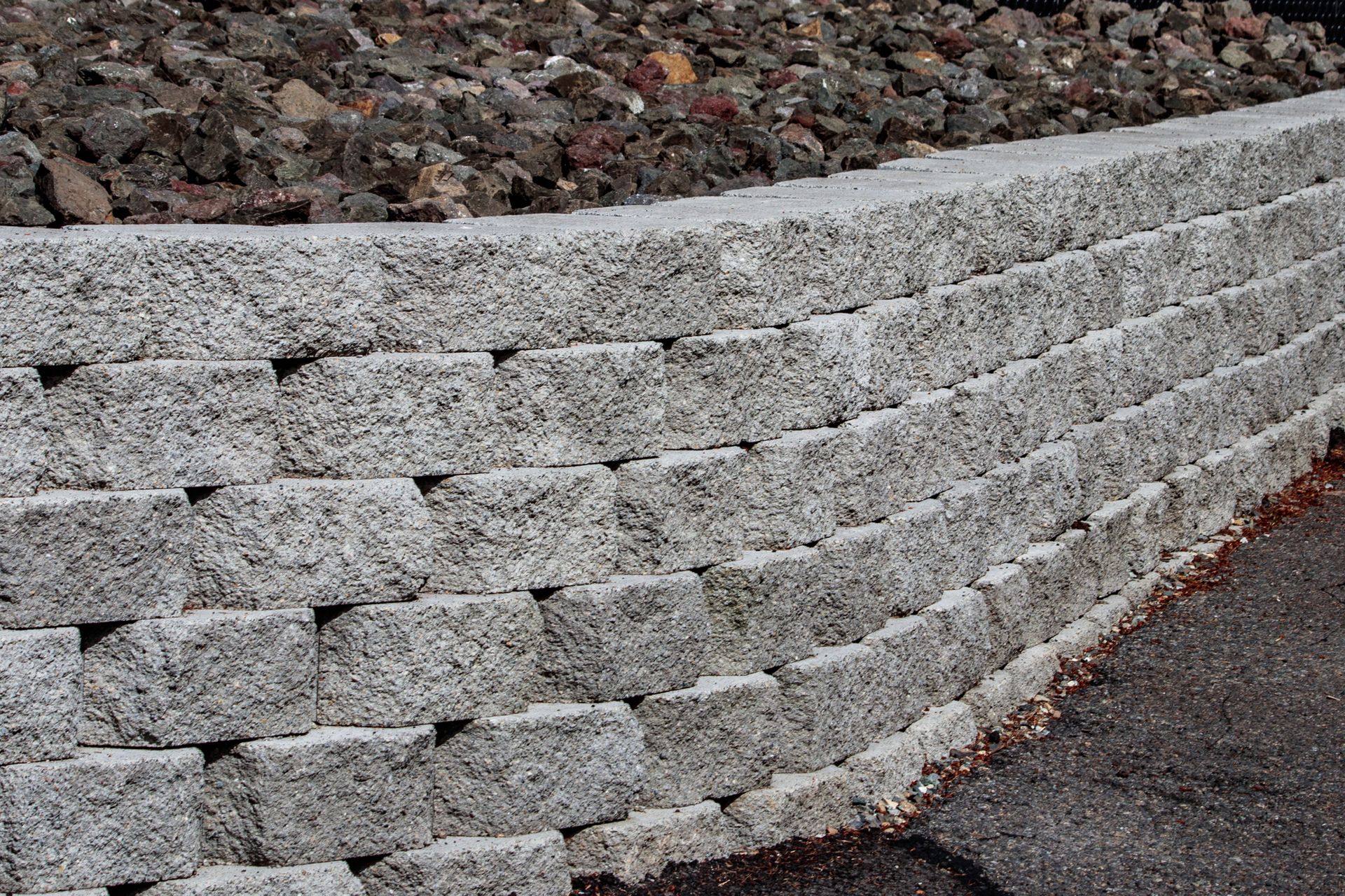 Stacked gray stone retaining wall along a roadside, with gravel above and pavement below