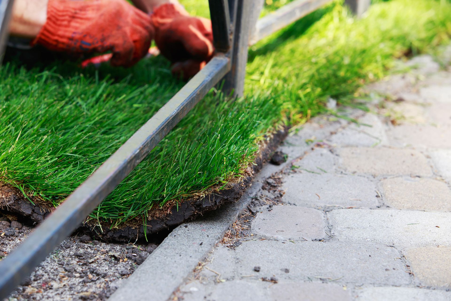 Worker trimming artificial grass along a paved edge with a metal tool