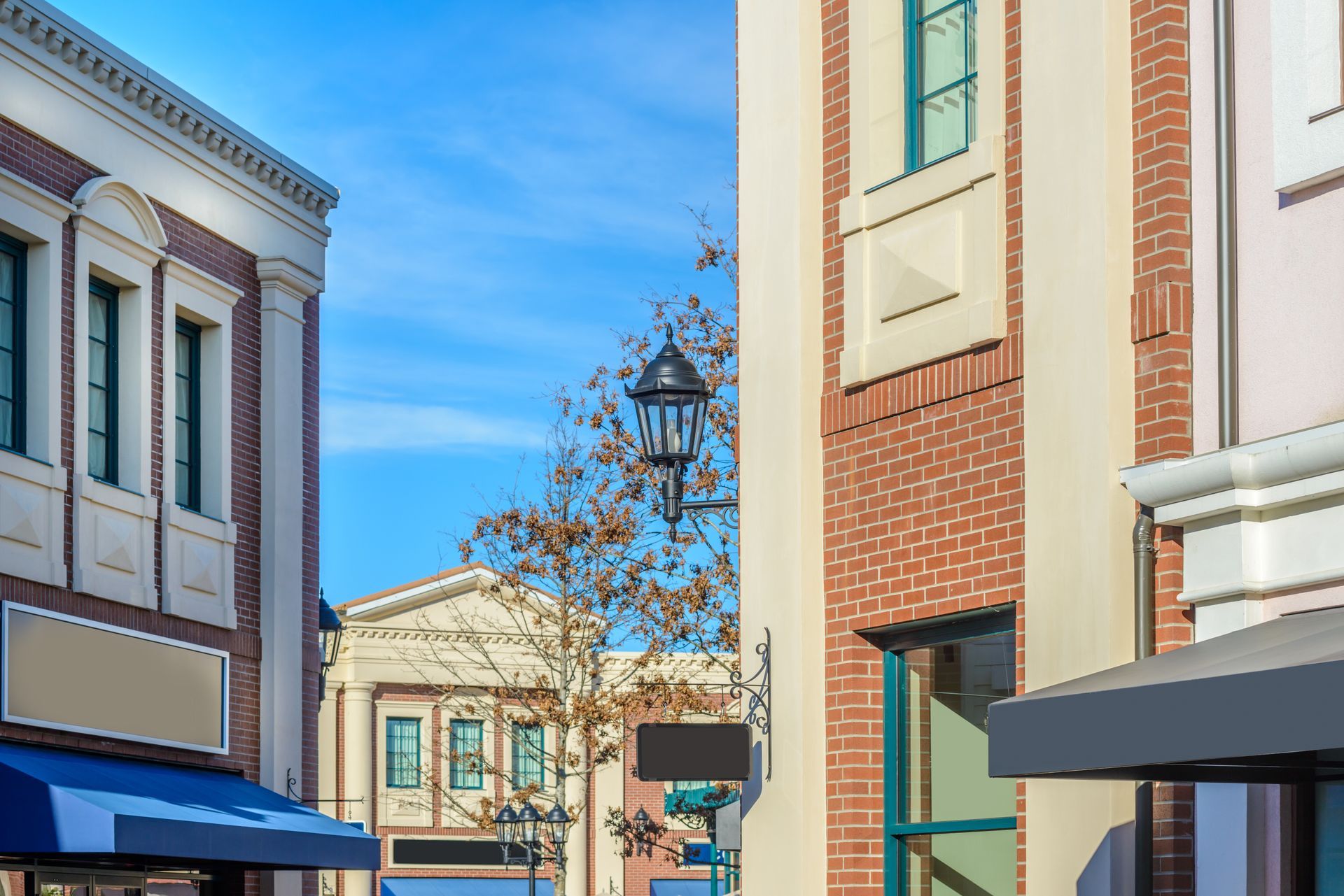 Sunlit street with pastel storefronts, brick buildings, and a blue sky between narrow shop-lined facades