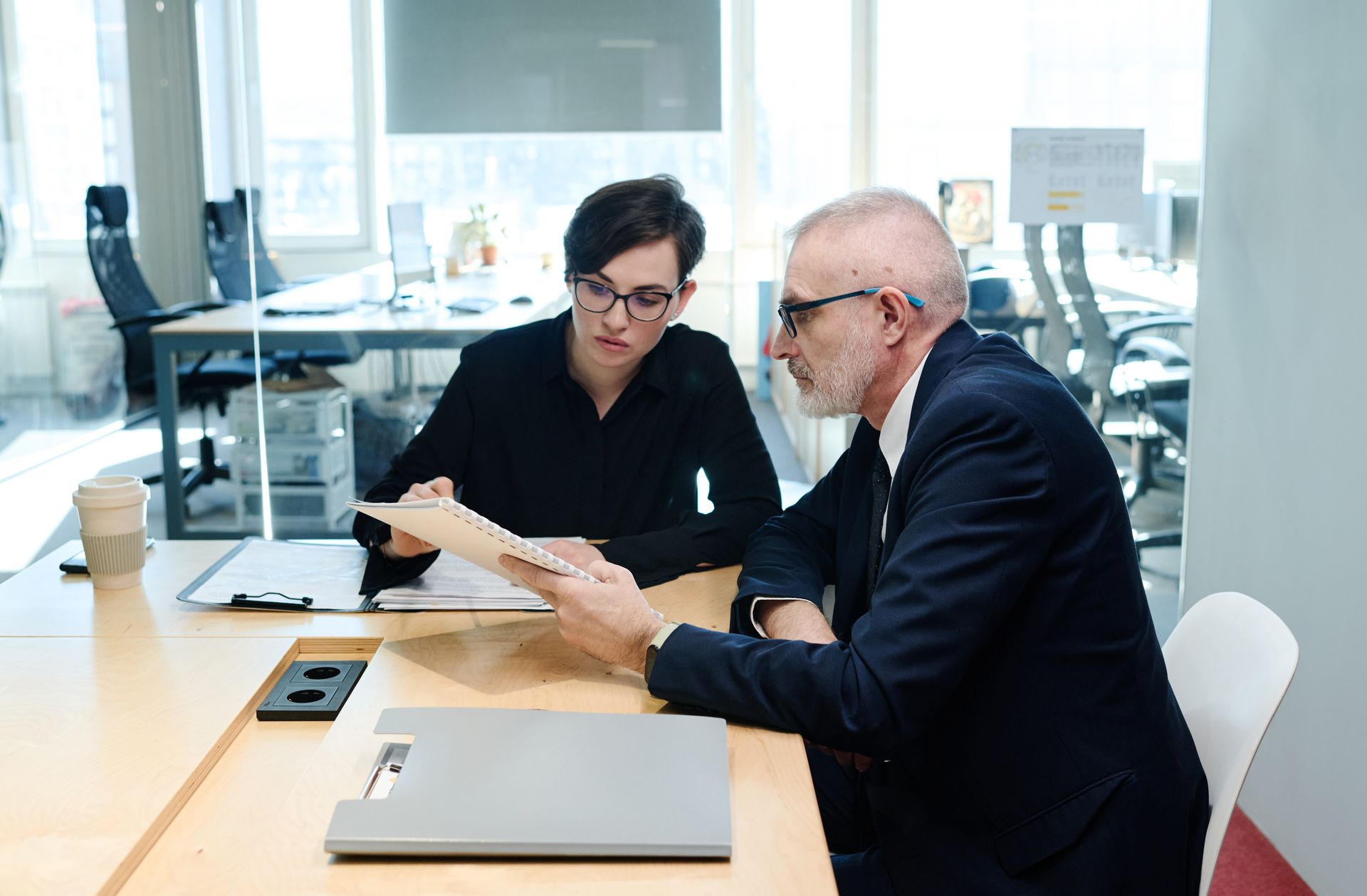 Two people reviewing documents at a conference table in a bright office
