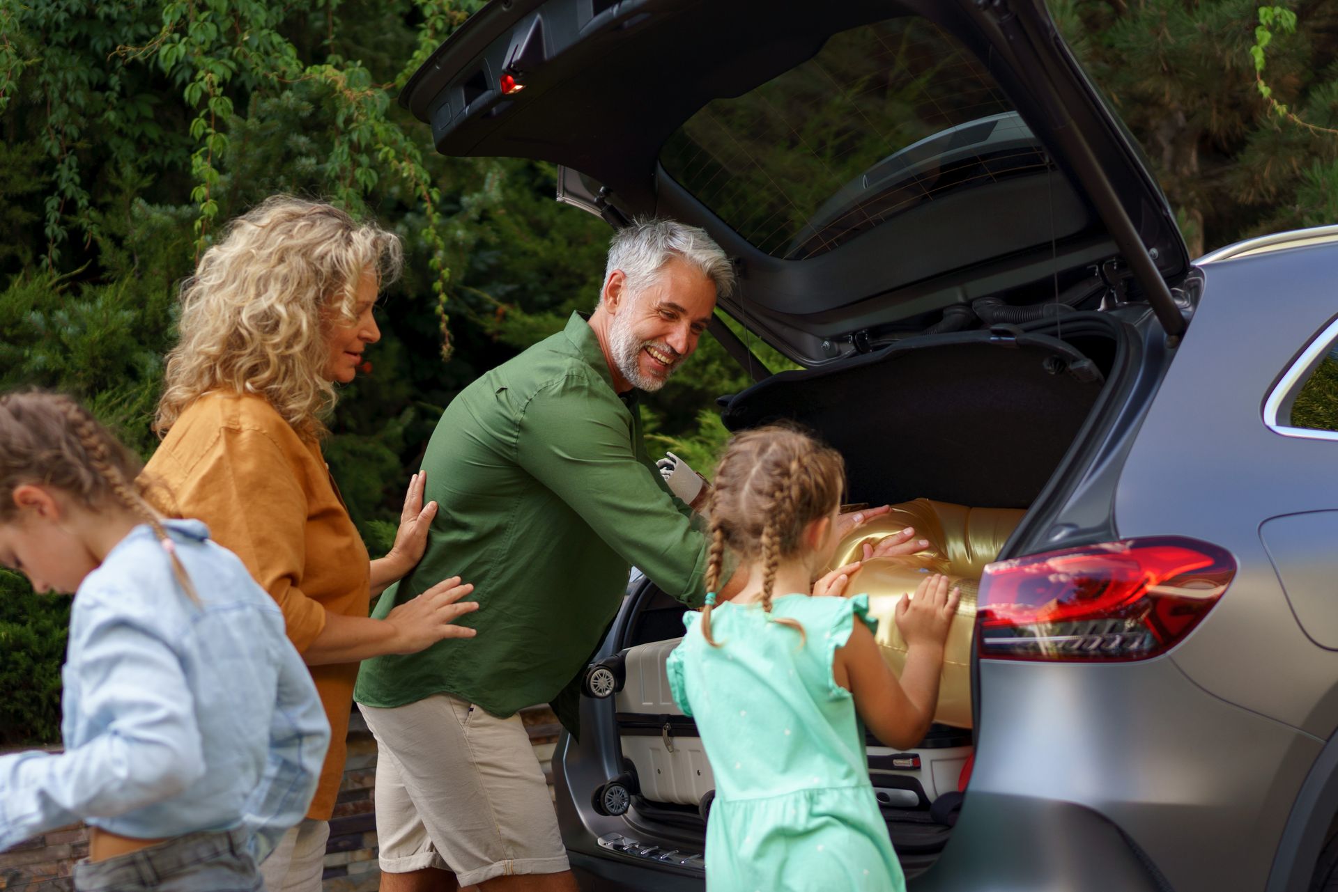 Family loading luggage into SUV with open trunk outdoors