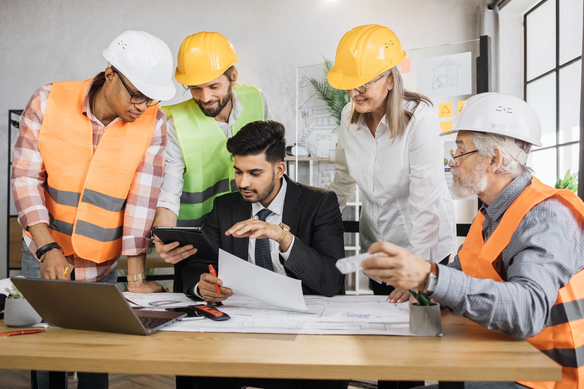 Construction team reviewing plans around a laptop and tablet at a desk in a worksite office