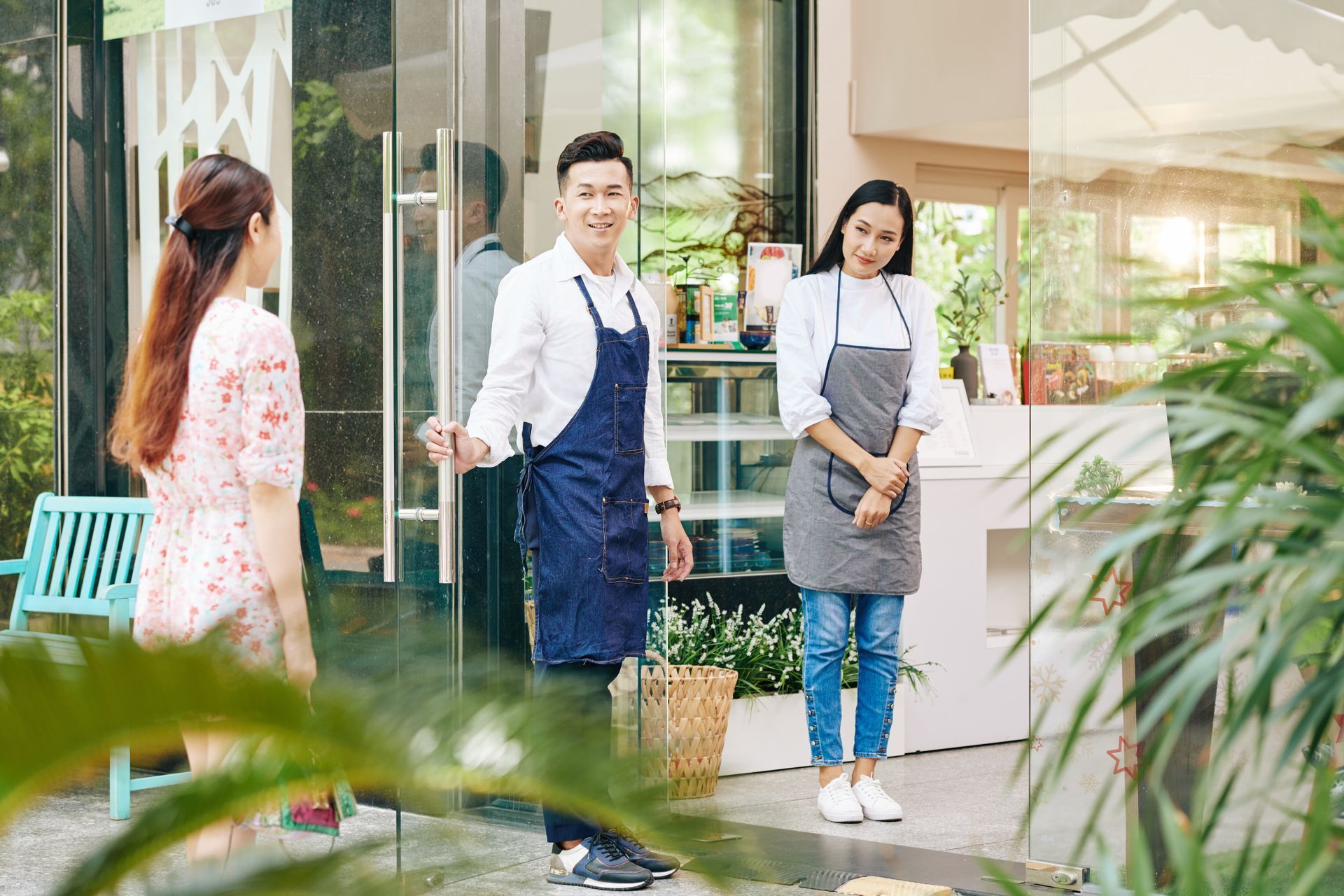 Three people outside a cafe: a man in an apron opens the door as two women arrive.