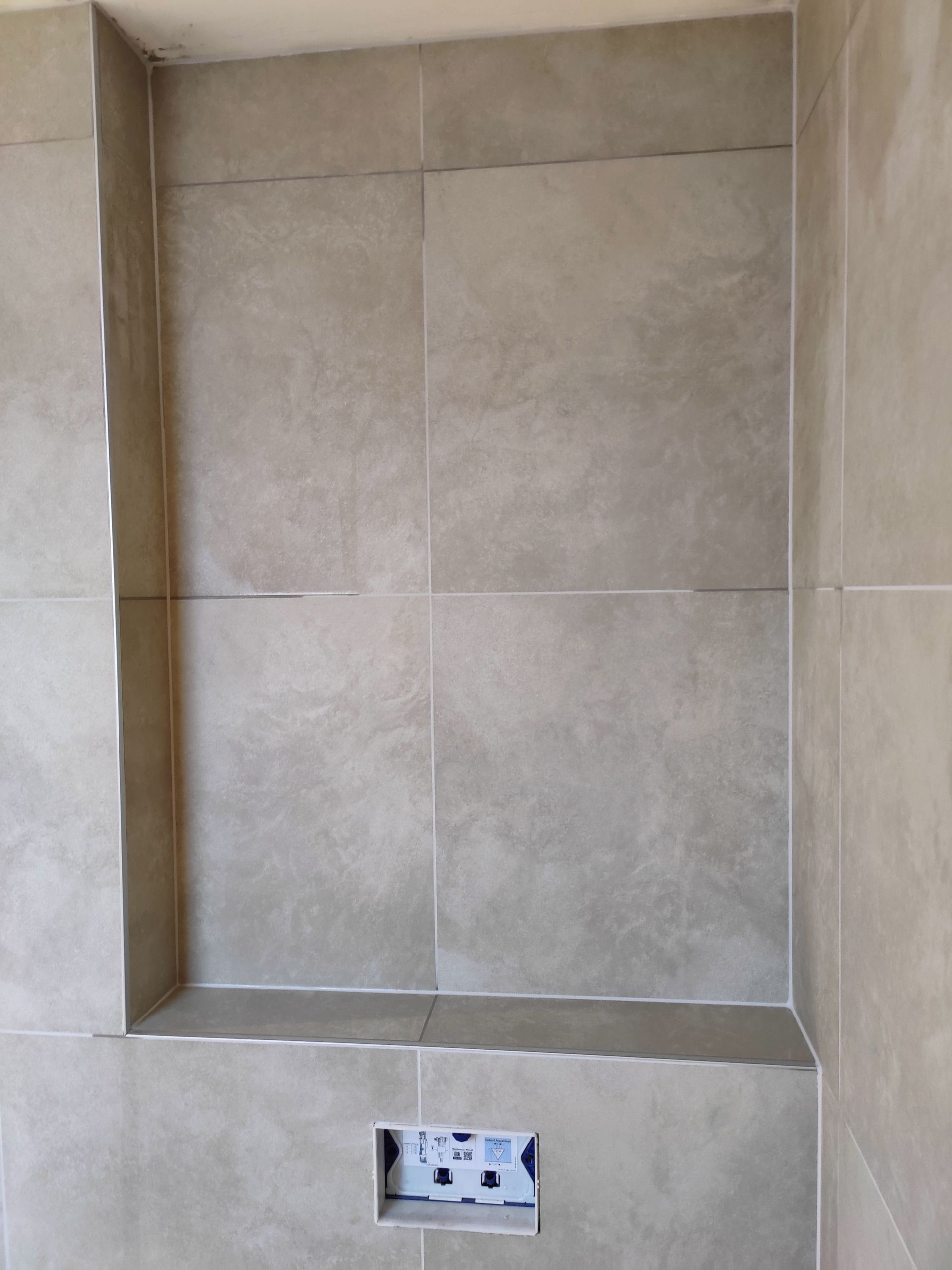 A tiled wall with a shelf in the middle of it