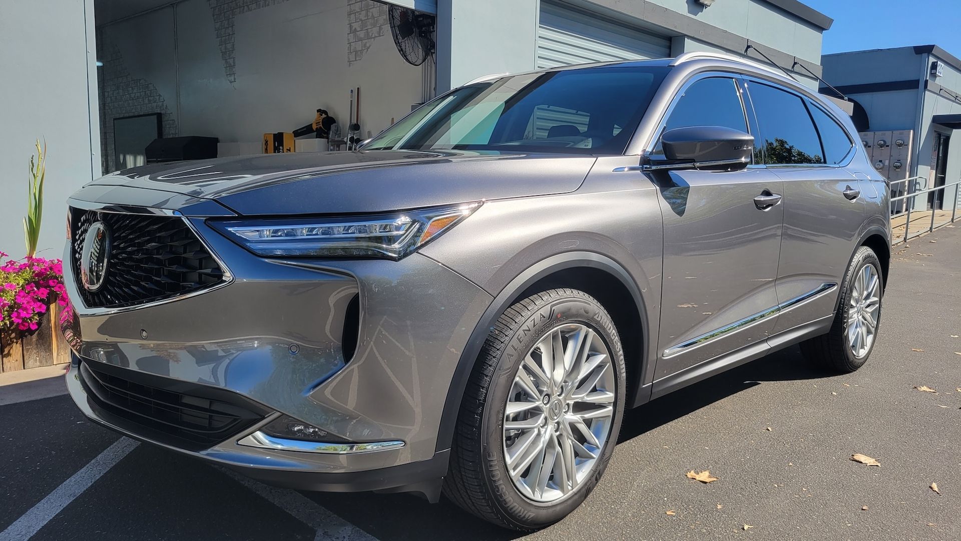 A gray acura mdx is parked in a parking lot in front of a garage.