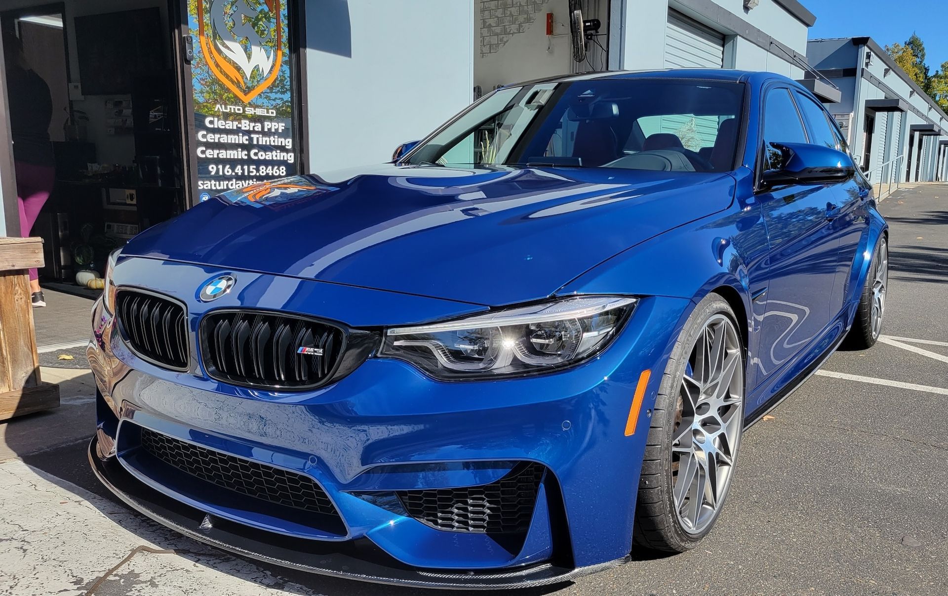 A blue bmw m3 is parked in a parking lot in front of a building.