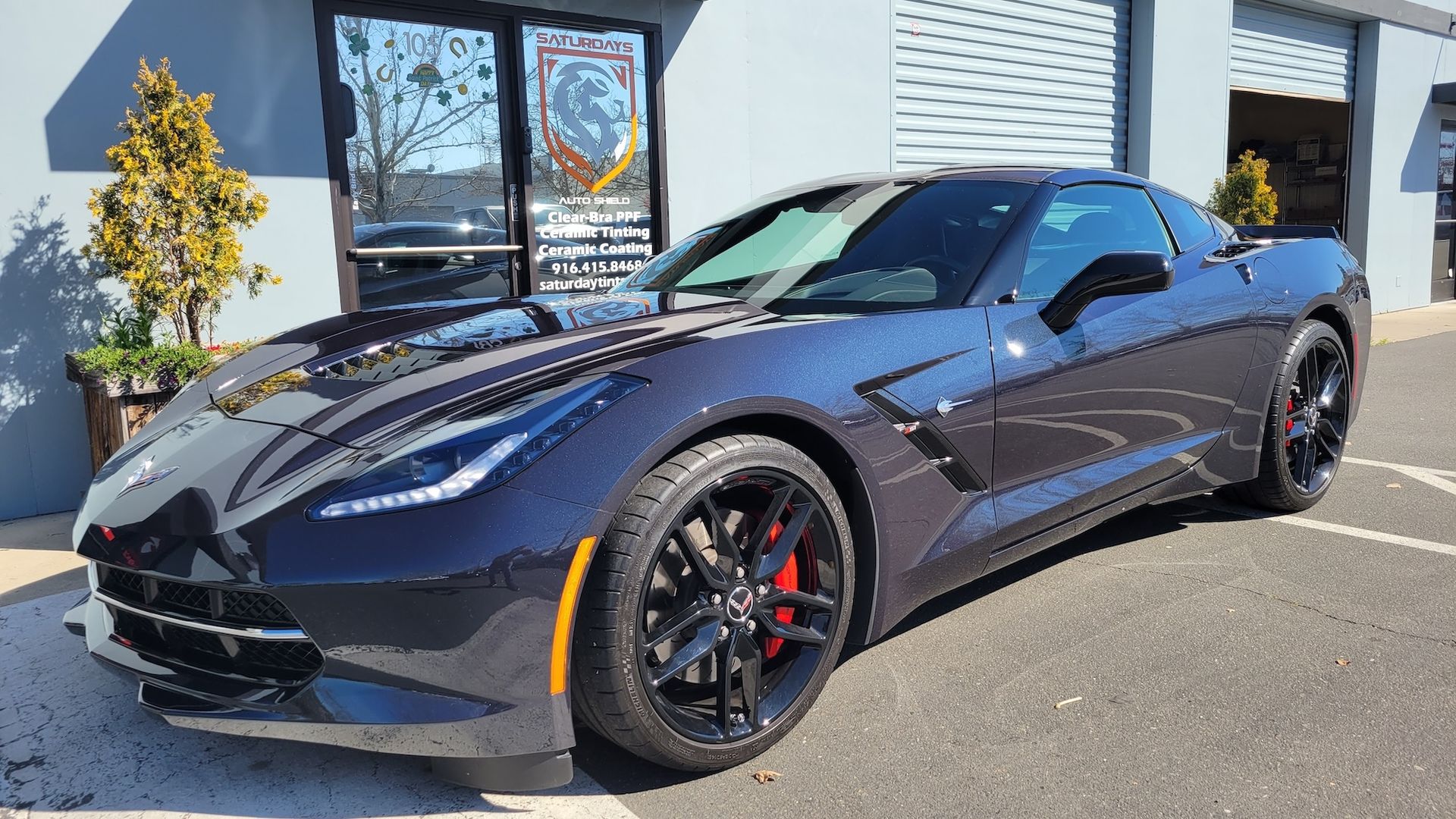 A blue corvette is parked in front of a building.