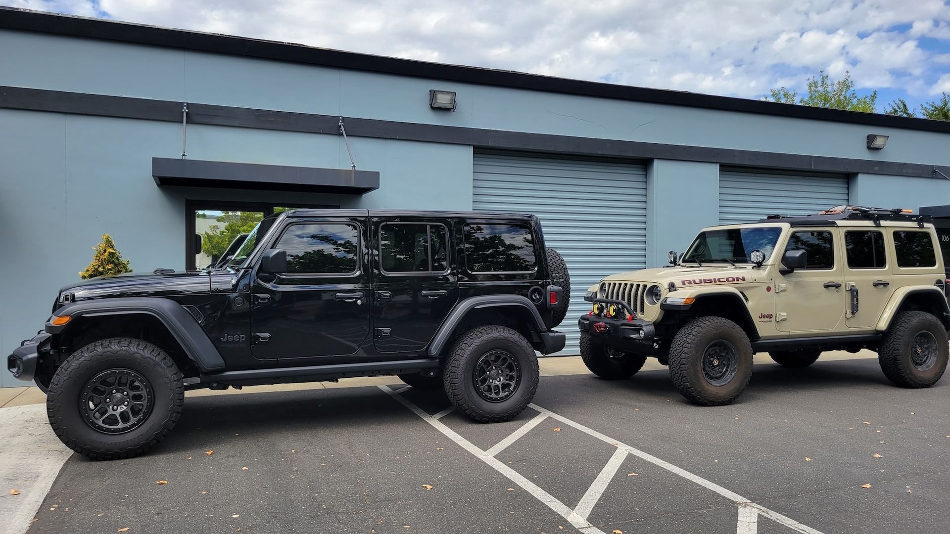 Two jeep wranglers are parked in a parking lot in front of a building.