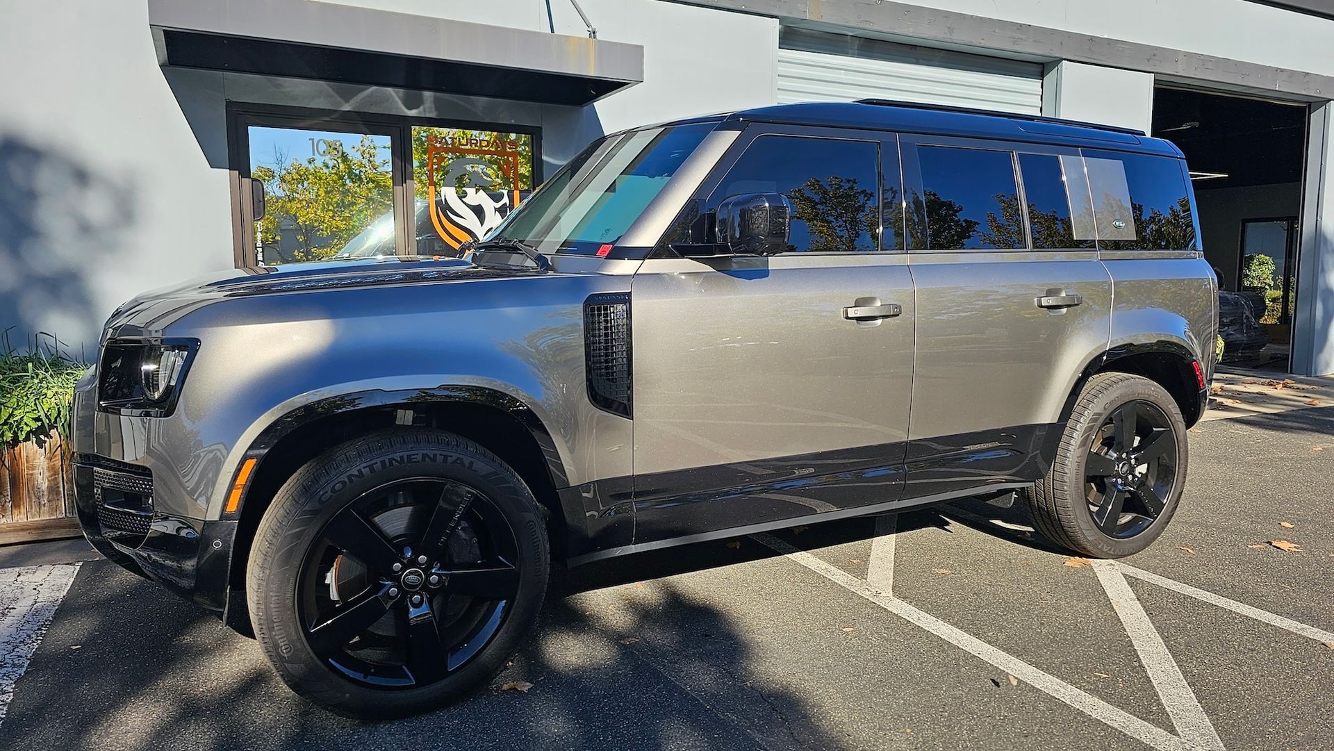 A silver land rover defender is parked in a parking lot in front of a building.
