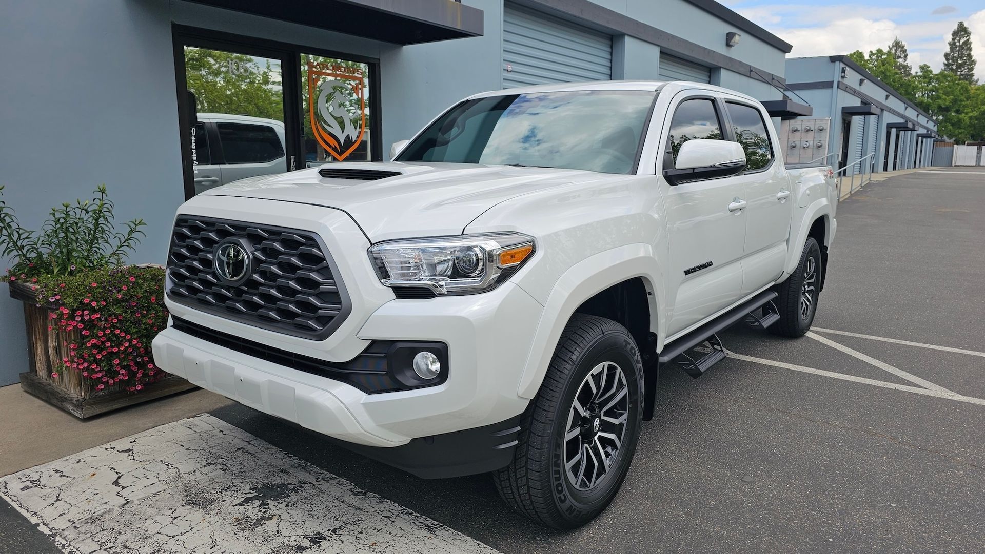 A white toyota tacoma truck is parked in front of a building.
