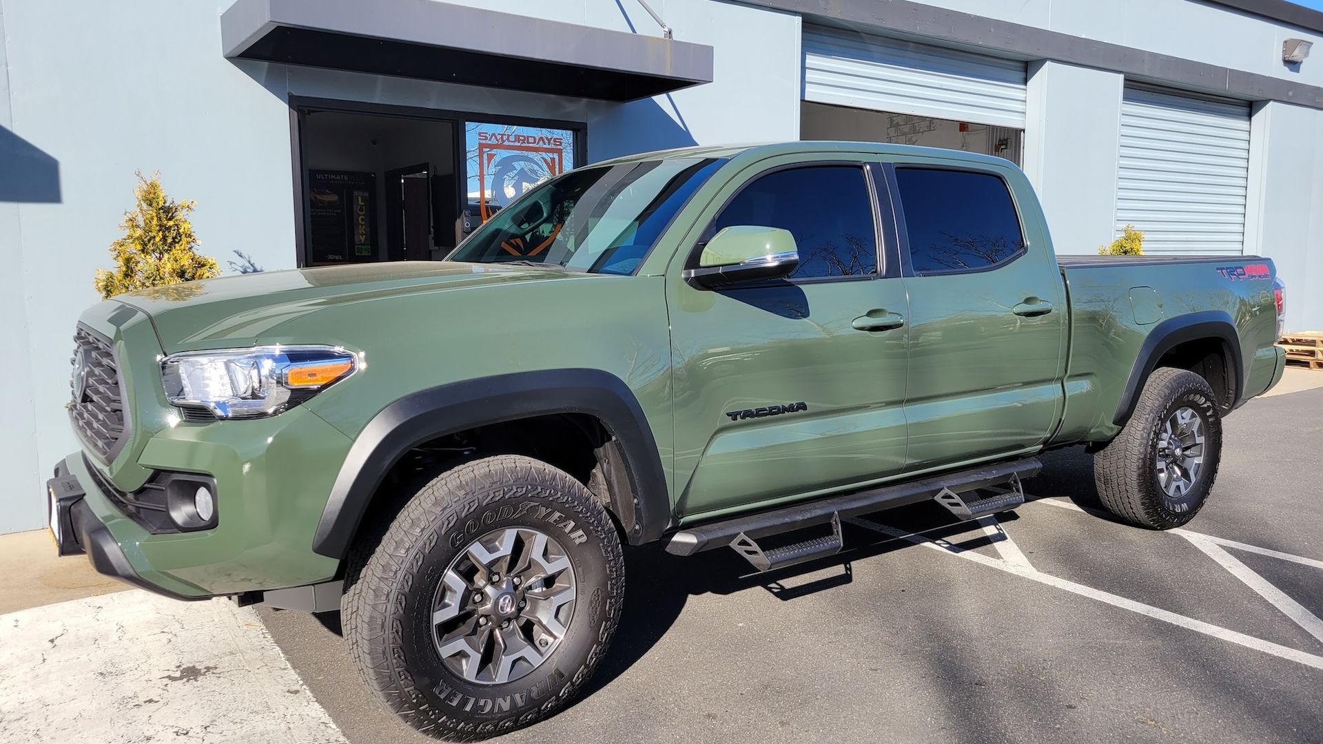 A green toyota tacoma truck is parked in a parking lot in front of a building.