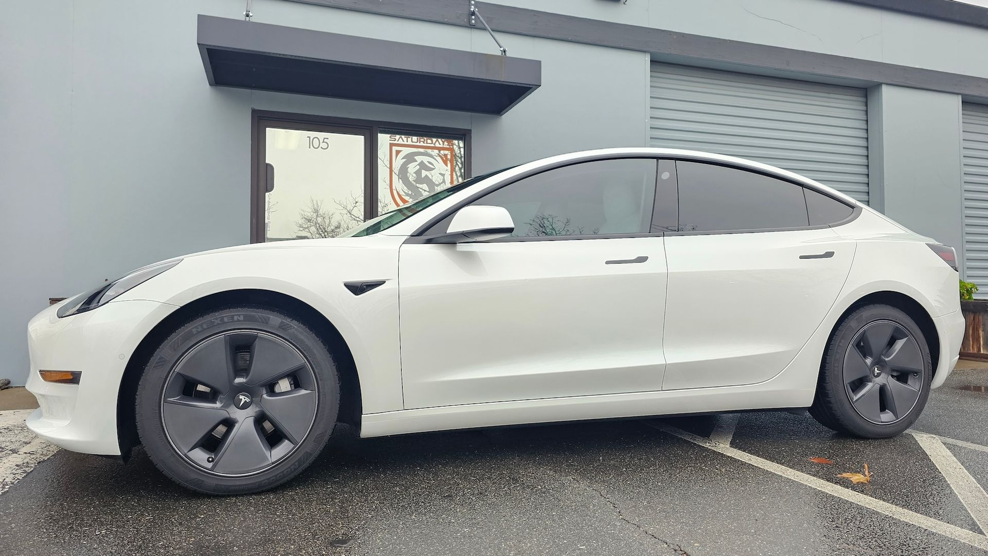 A white tesla model 3 is parked in a parking lot in front of a building.