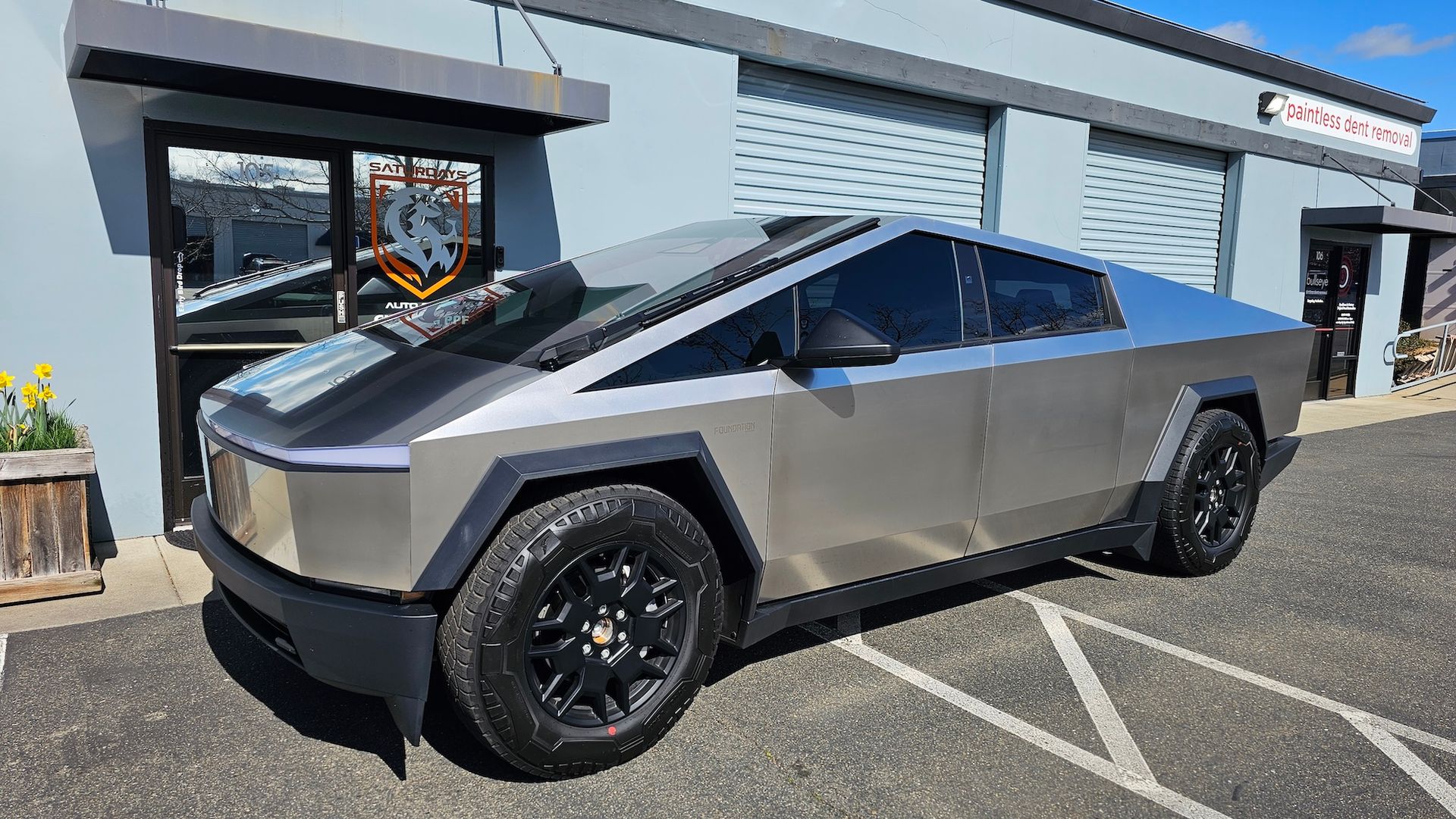 A silver tesla cybertruck is parked in front of a building.