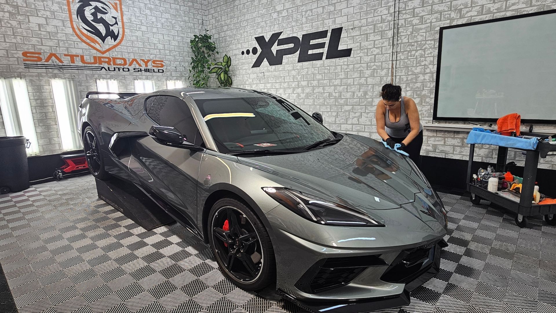 A woman is cleaning a gray sports car in a garage.