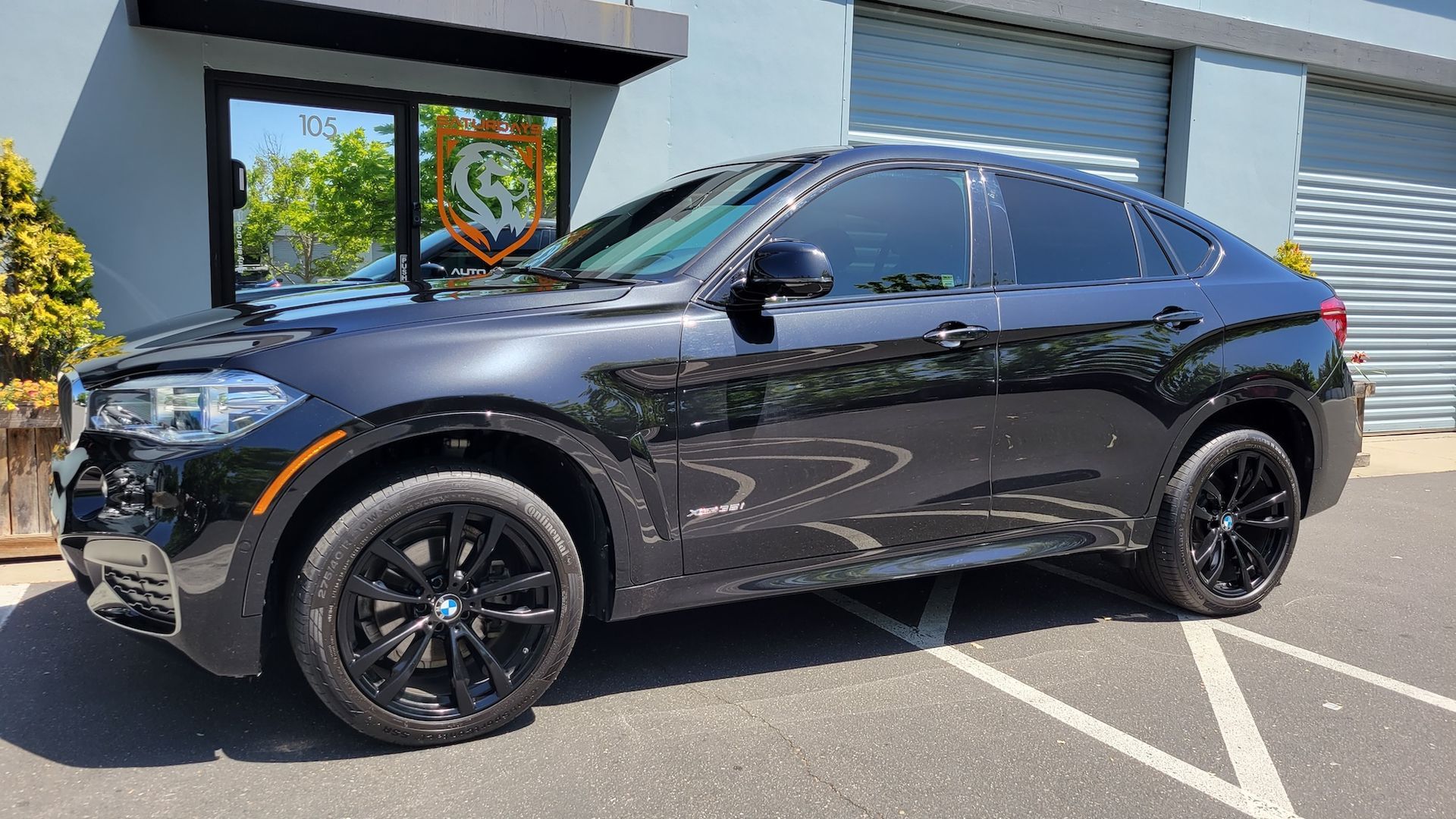 A black bmw x6 is parked in a parking lot in front of a building.