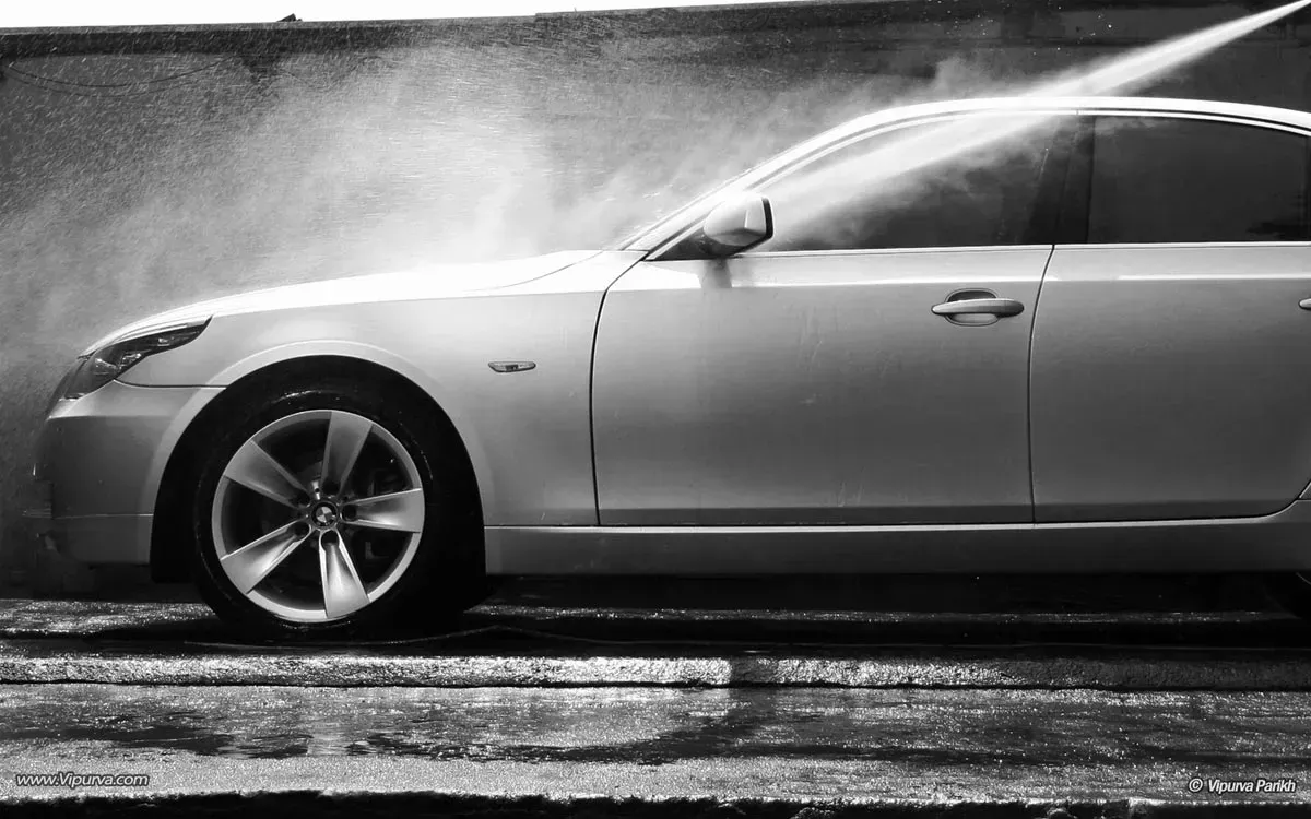 A black and white photo of a car being washed with a high pressure washer.