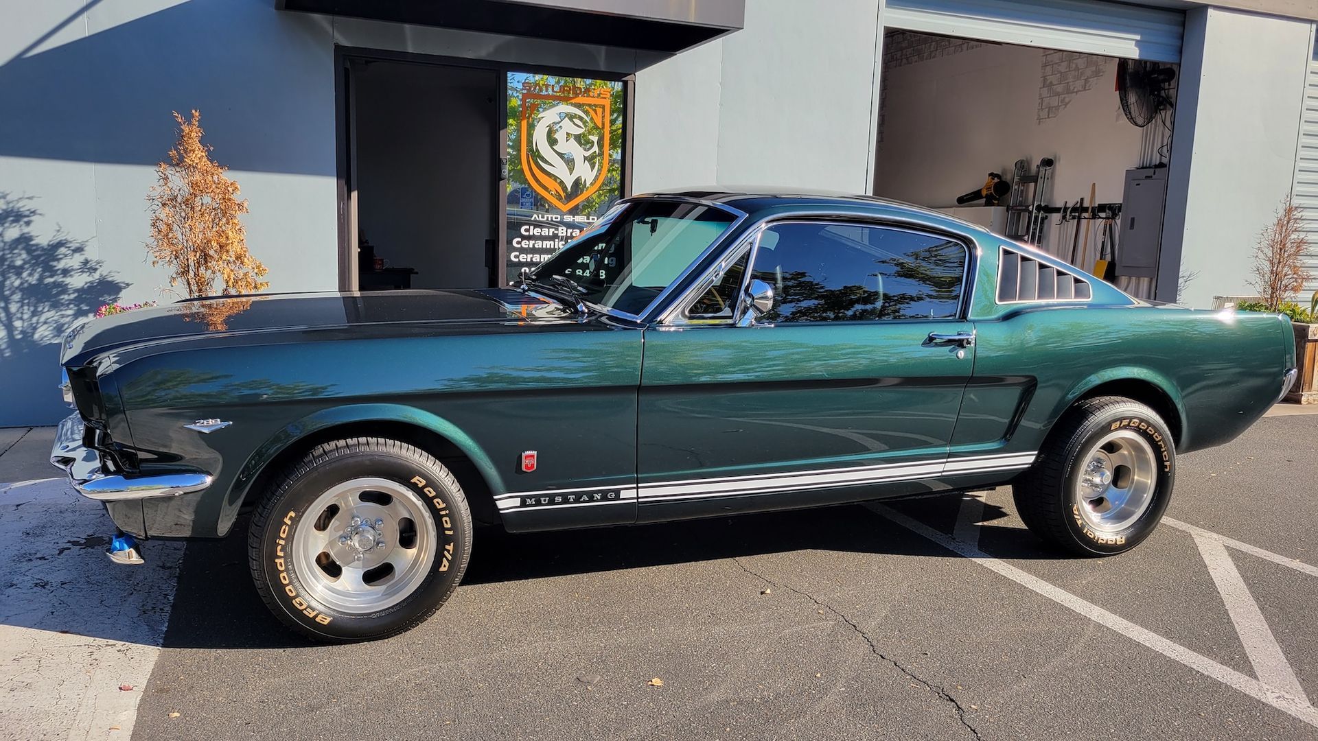 A green mustang is parked in a parking lot in front of a garage.