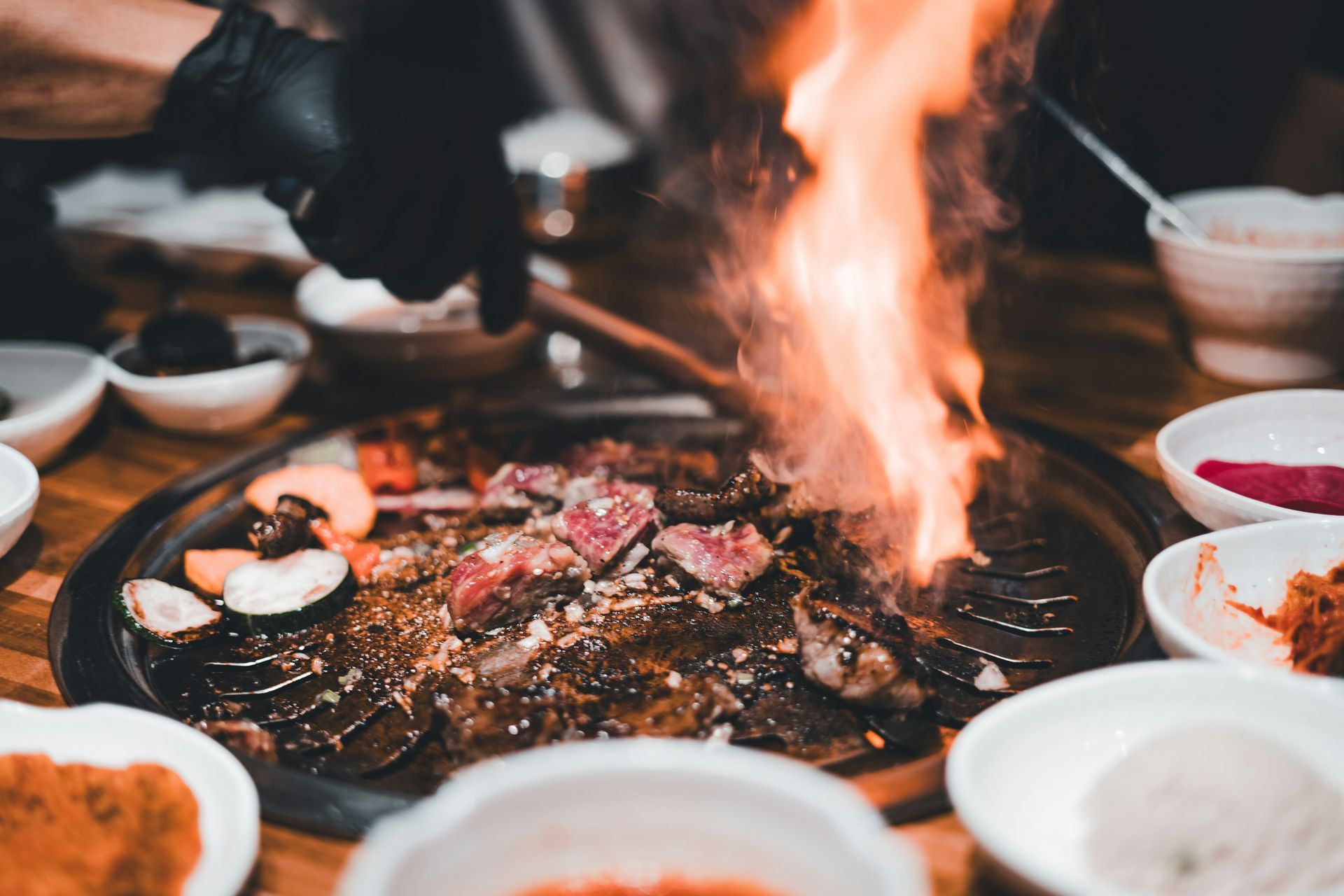 Une personne fait griller de la viande sur une plaque chauffante, les flammes s'élevant.
