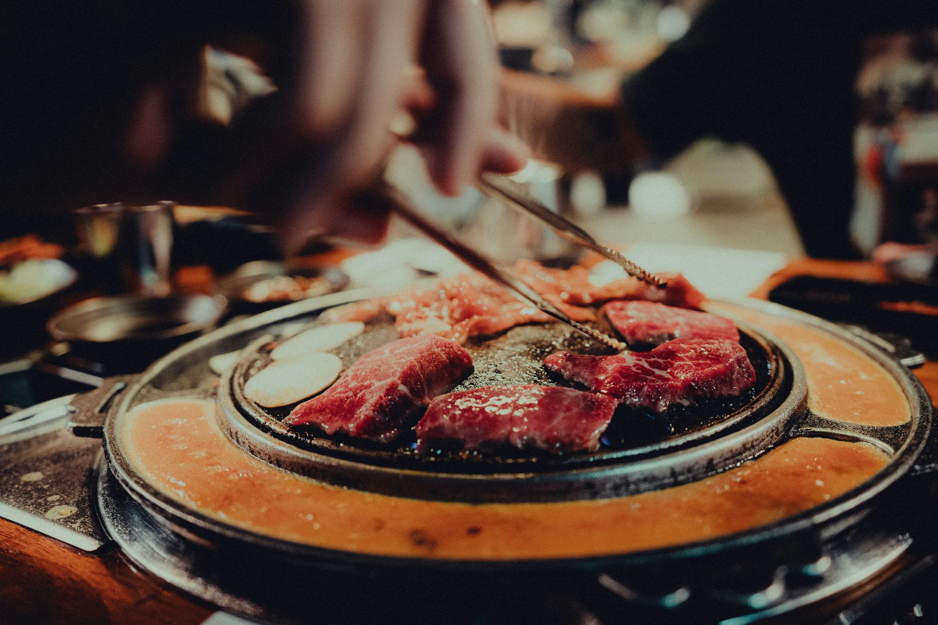 Repas de barbecue coréen avec de la viande grésillante sur une plaque chauffante, servie à la main avec des pinces.