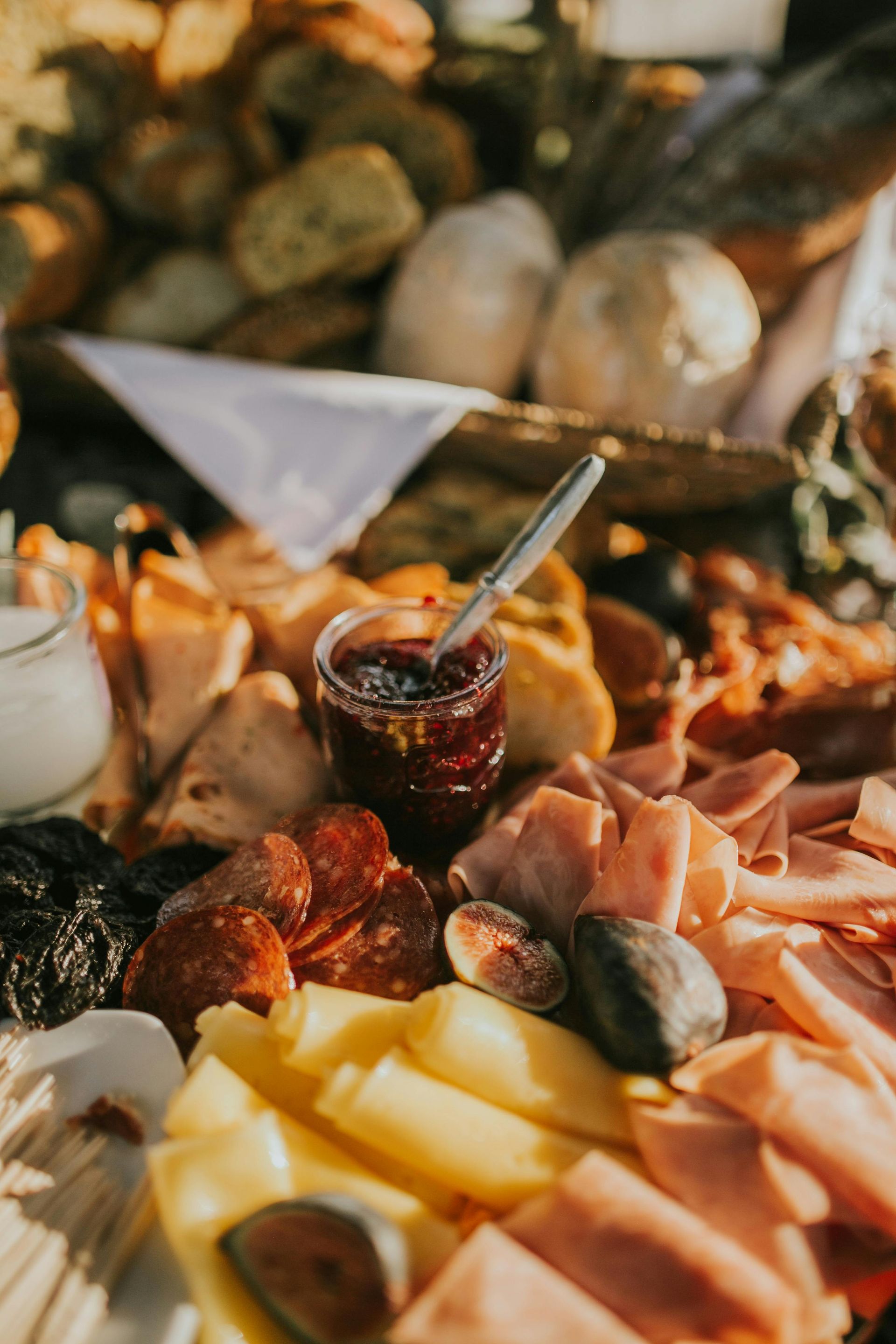 Planche de charcuterie : viandes, fromages, confitures, figues, pain et condiments, en extérieur.