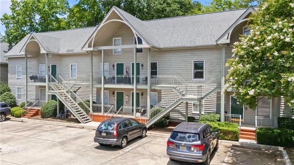 Apartment building with white siding, front stairs, and two parked cars in a tree-lined lot