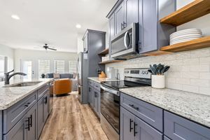 Bright modern kitchen with blue-gray cabinets, white countertops, stainless appliances, and a view into the living area