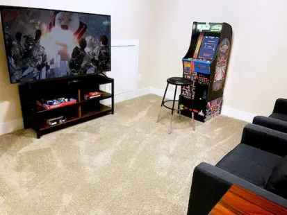 Living room with a large TV on a stand and an arcade game machine beside a couch.
