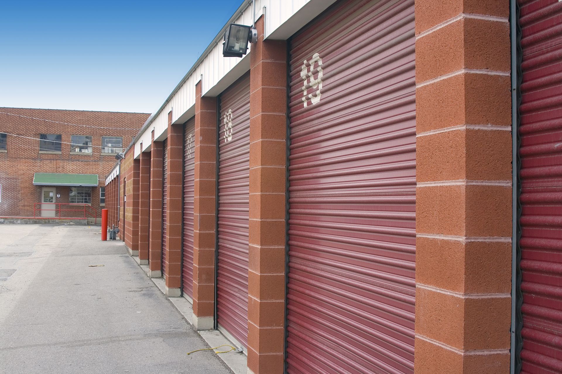 Red storage unit doors with brick columns, concrete path.