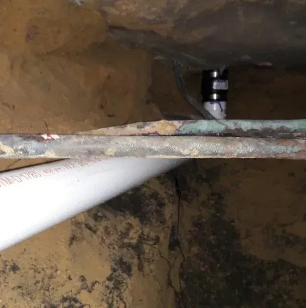 Close-up of a rusty pipe inside a narrow dirt-covered opening.