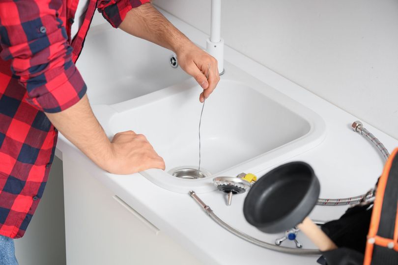 Person cleaning a white sink with running water, tools nearby on the counter