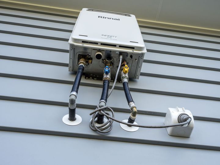Outdoor wall-mounted utility box with exposed cables and pipes on a gray siding wall