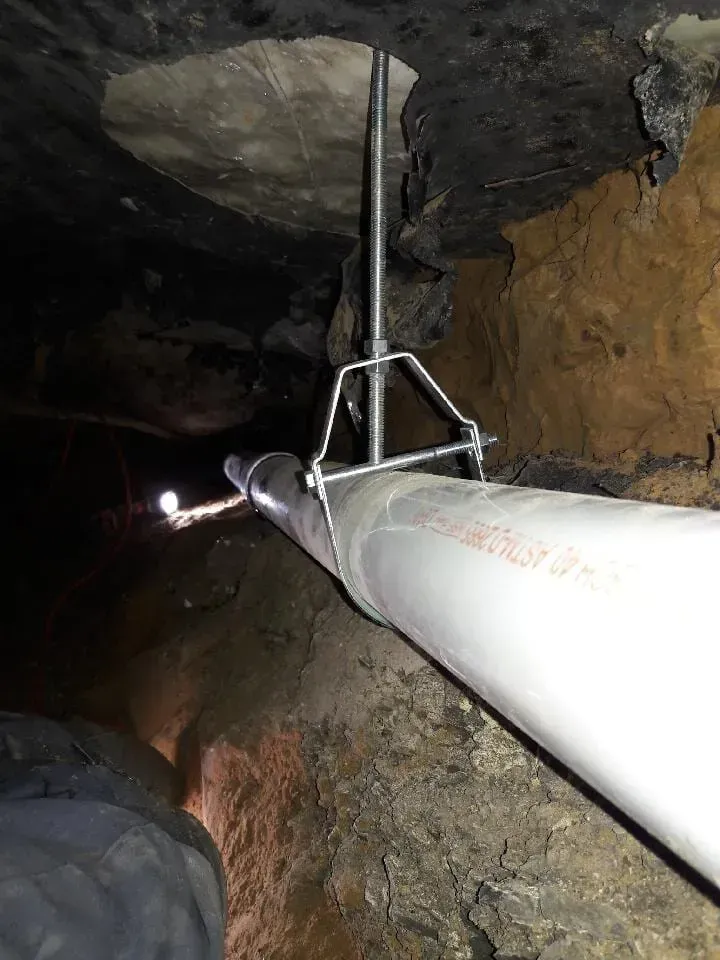 Mineral pipe with clamp in a narrow rocky tunnel, viewed from inside a cave