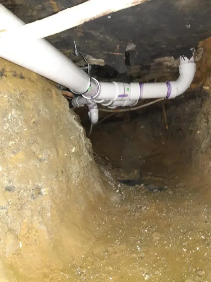 White PVC pipes inside a dark dirt crawlspace or trench under a structure