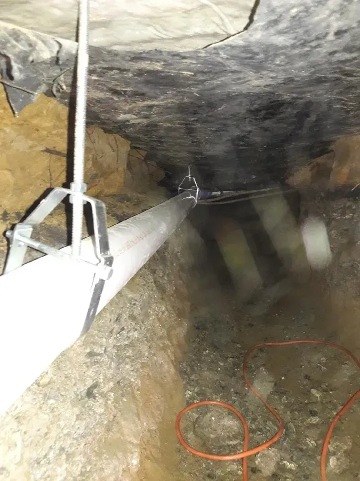 Narrow underground tunnel with pipes along the wall and cables on the wet floor