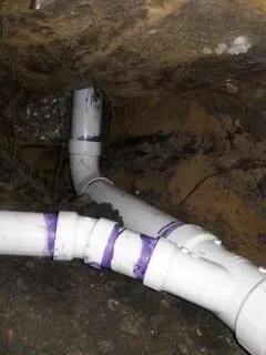 White PVC pipes with purple tape running through a dirt trench underground