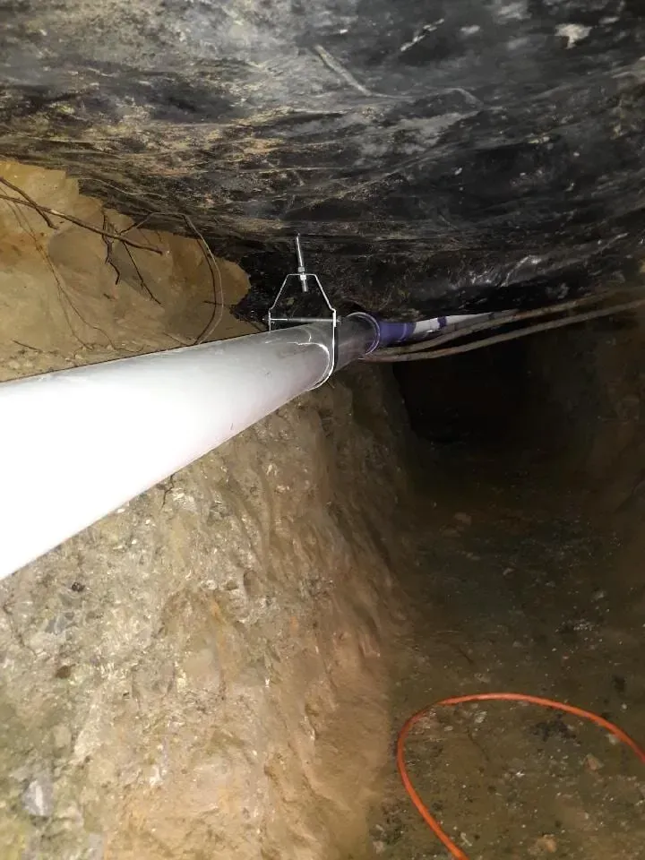 White pipe in narrow underground tunnel with rock walls and a cable loop on the floor