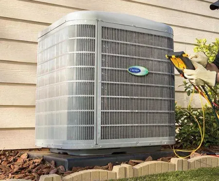 Outdoor air conditioner unit beside a house, with a worker using tools nearby.