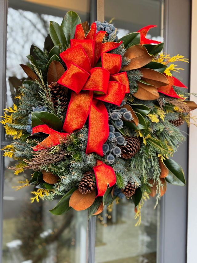 Red holiday wreath with bow and berries on a glass door