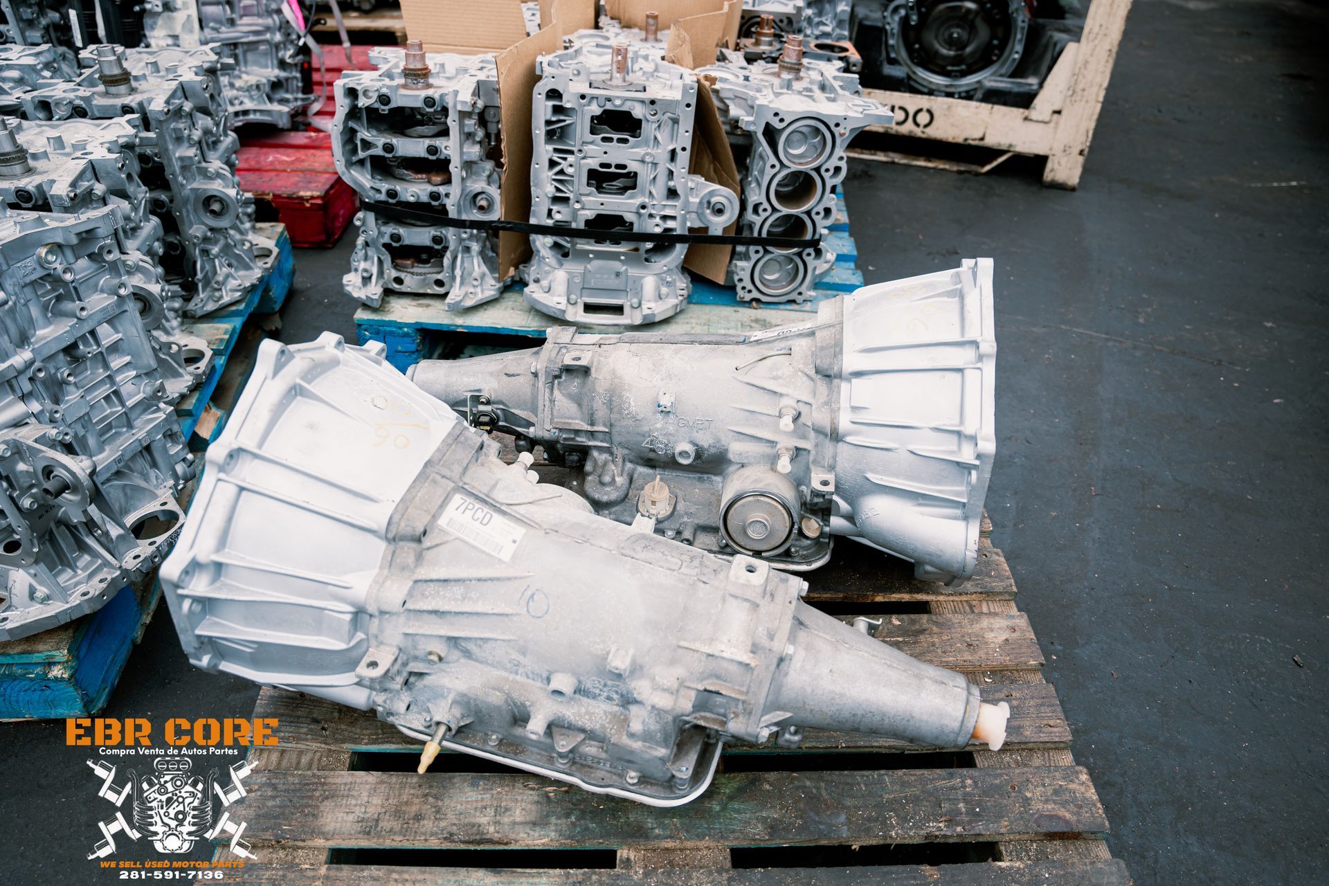 Car transmissions and engine parts on pallets in a warehouse, silver metal.