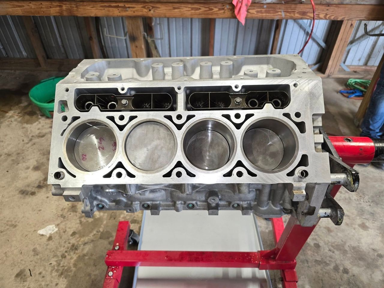 Engine block with pistons inside on a red engine stand, indoors.